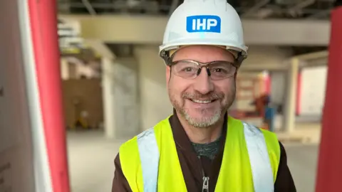 Image of Kevin Clark. He is pictured inside the hospital, wearing a hi-vis vest and hard hat.