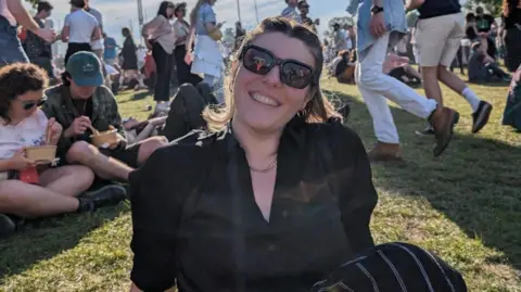 Jess Warren/BBC Jess sat on the grass at a festival