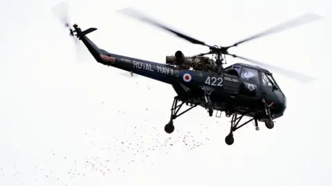 PA Media Poppy petals are dropped from a Wasp helicopter off the coast of Portland in Dorset,