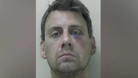 Mugshot of Benjamin Ypma. He has a short scruffy goatee and thick black hair. He has a large bruise under his left eye.