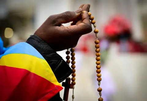 Tizyana FABI / AFP, a woman wrapped in the State flag of the Democratic Republic of the Congo, Gemelli University Hospital, where Pope Francis was hospitalized with Pennemony, praying the statue of John Paul II.