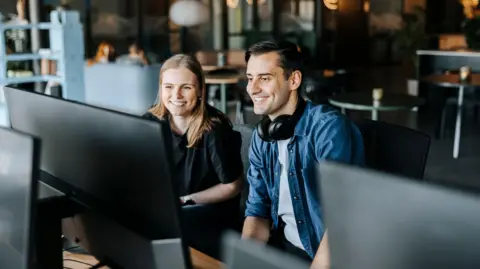 Happy male and female entrepreneurs watching computer screen sitting in tech startup office - stock photo