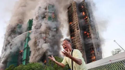 Reuters A man gestures in distress as the tower blocks burn behind him.