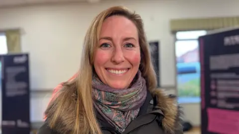 Local resident Vikki Wallace is pictured smiling. She has long blond hair and a multi-coloured scarf and green parka coat