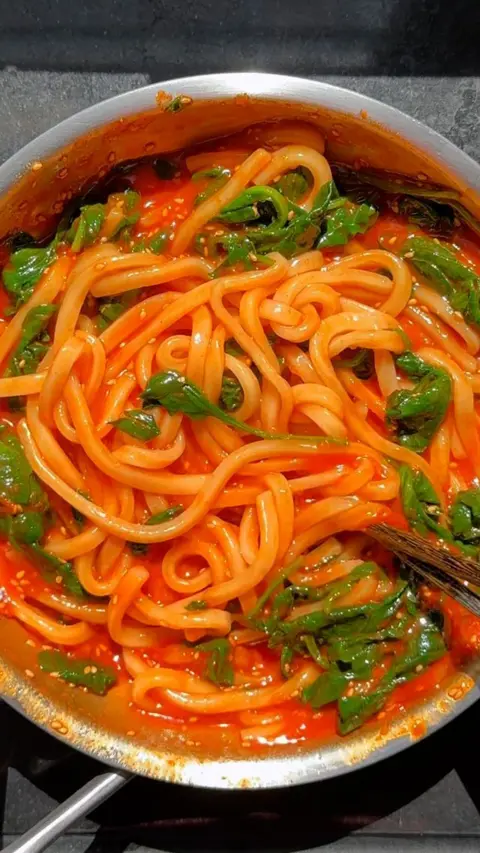 Bowl of orange Spicy gochujang udon noodles with green spinach 