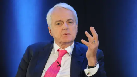 Sir Robert Francis, wearing a blue suit jacket, pink tie and white shirt 