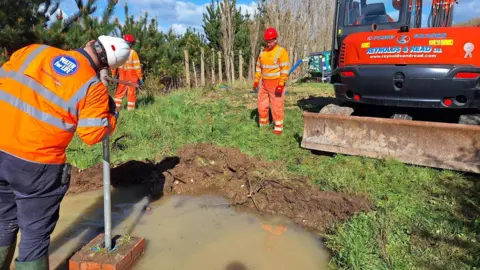 Southern Water workers standing in a flooded field and a digger.