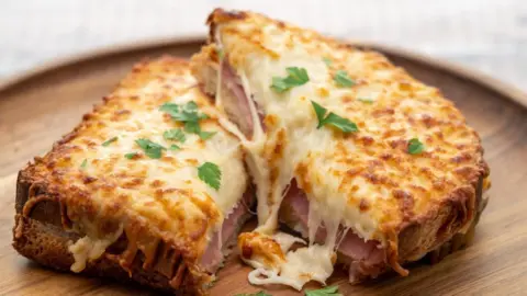 Clubfoto/Getty Images A croque monsieur, a sandwich with toasted bread, ham, and melted cheese on top with parsley, in served on wooden plate