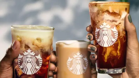 Close up of people's hands as they hold up three different Starbucks-branded drinks.