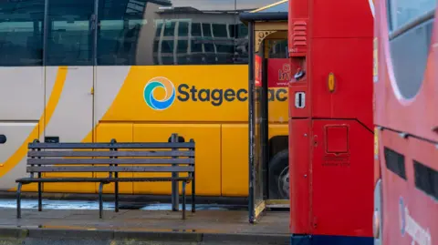 Close-ups of the sides of buses at Inverness bus station. There is a yellow and white Stagecoach bus and parked near it a red bus.