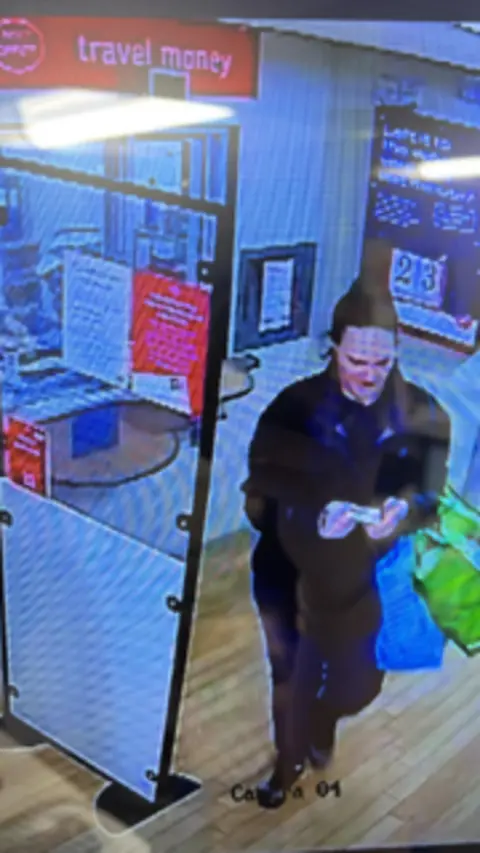 Supplied CCTV footage of Lisa Harper leaving a post office. She is carrying a number of plastic bags in one arm and is wearing a black tracksuit. She is standing near a plastic divider near the post office counter.