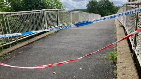 BBC/Phil Bodmer Police and emergency services tape cordons off a footbridge. 
