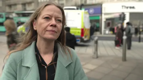 Ian Palmer / BBC Sian Berry, a woman stood in a small city centre plaza. She is stood in front of a police van.