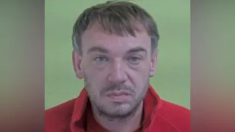 ISLE OF MAN CONSTABULARY Police photo of Ross Beggs-Cairney, who has short brown hair and stubble and is wearing a red fleece top.