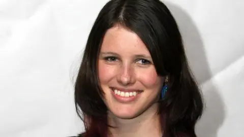 PA Media Josie has brown, shoulder-length hair and is smiling at the camera