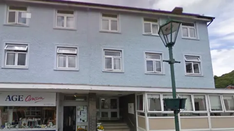 Google The outside of Moot Lodge which is pale blue and above an Age Concern shop