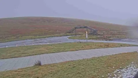 A view of the Mountain Road, there is some snow on the grass, you can see a bridge to cross the route.