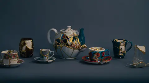 UK for UNHCR Six pieces of pottery are on display, including cups and a teapot. They have clearly been broken and repaired using gold, a Japanese technique called Kintsugi.