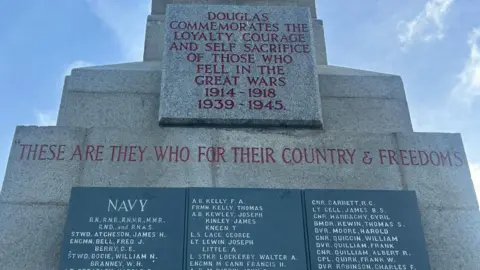 A closeup of the Douglas war memorial, which has three piece of black marble listing the names of some of those killed. The words Douglas commemorates the loyalty, courage, and self sacrifice of those who fell in the Great Wars 1914 - 1918 and 1939 - 1945 are inscribed in red lettering on the monument above the black slabs.