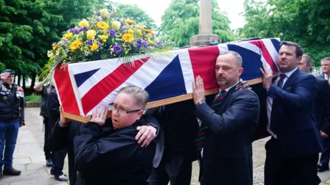 James Kirby's family and friends carrying his coffin into the church - it has a union jack flag and flowers over it