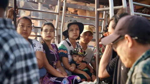 Lulu Luo/ BBC Three women, one holding a child in her lap, and a man seen on a bus in Yangon 