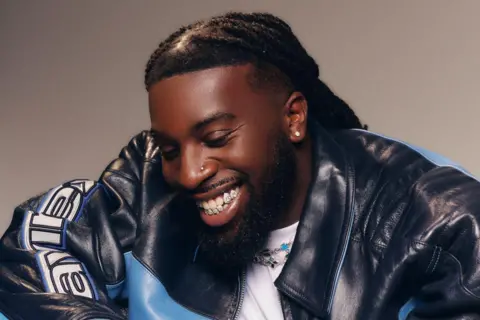 Family handout Mark Orabiyi looking down smiling. He is wearing a black and blue leather jacket over a white T-shirt