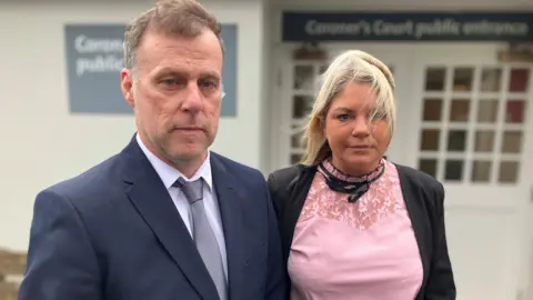 Allyn and Jenny Condon - him in a navy suit and her in a pink top and black blazer, standing outside the court