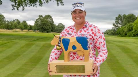 Alice Hewson holds up the trophy for winning the Swiss Open - a wooden carved cow