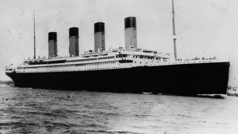 Black and white photo of the four-funnelled Titanic ship on water.