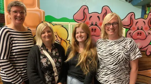 Four women standing in front of a farmyard background in a children's play barn.