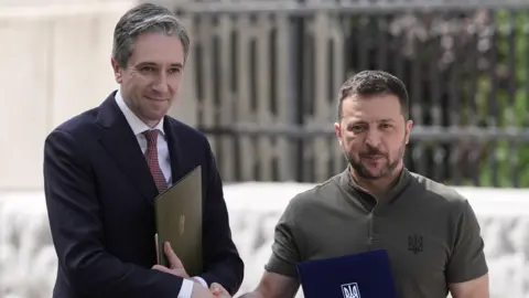 PA Media Simon Harris and Volodymyr Zelensky shaking hands and holding folders. 