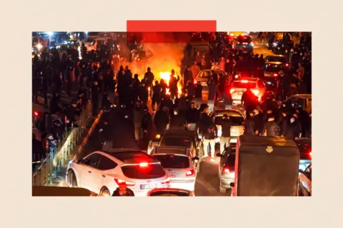 Getty Images Hundreds of people out on the streets protesting, with a bonfire in the distance and cars in the foreground