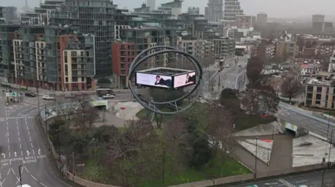 Current advertising structure shows screen in orb on roundabout with cars, bus and lorry