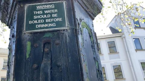 An old water pump in Guernsey. A sign reads: Warning - This water should be boiled before drinking.
