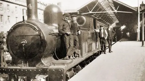 Jim Lake Collection/disused-stations.org.uk A black and white image of a steam train with four men standing next to an engine on a platform.