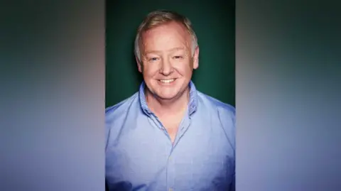 Aylesbury Waterside Les Dennis head shot. He is smiling and wearing a blue shirt