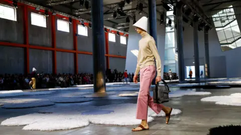 Reuters A model wearing pink pants and a beige top presents a creation from Prada Spring-Summer 2026 menswear collection during the Milan Fashion Week in Milan, Italy, June 22, 2025.