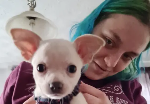 Family photo Rebekah Morris in burgundy top with chihuahua. They are both looking directly at the camera.