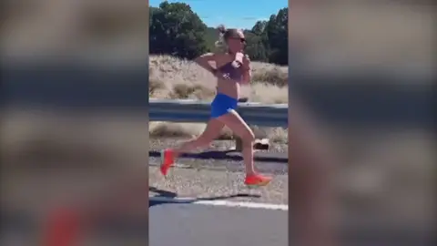 Calli Hauger-Thackery mid-stride during a run, wearing a purple crop top, blue shorts and orange trainers