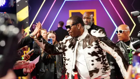 PA Media Busta Rhymes in a black and white cowpring leather jacket and high-fiving a fan