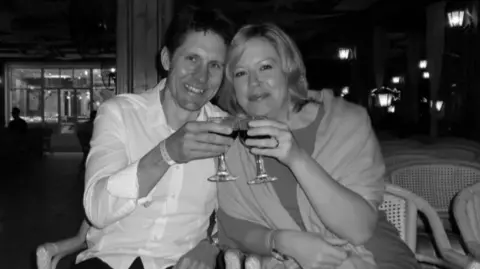 Jodie Smith A man and a woman are making a toast with their wine glasses. They are pictured in a black and white photo. The man is wearing a white shirt and has short hair. The woman is wearing a dress with a shawl over her shoulders.
