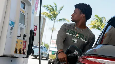A man looks at the price meter while refuelling his car at a petrol station 
