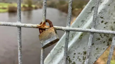 A rusting padlock sits on the railing of Gower Bridge in Llanrwst