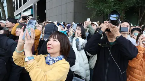 Getty Images Onlookers take pictures and record footage of US rock climber Alex Honnold climbing the Taipei 101 building. People are holding a variety of devices, including mobile phones and cameras. 