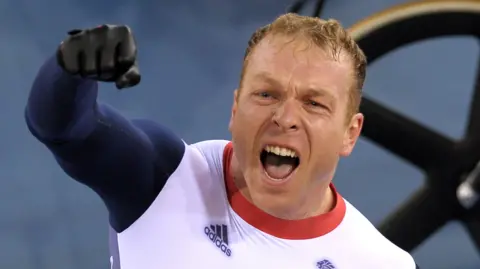 Sir Chris Hoy punches the air with his right hand after winning a race at the London 2012 Olympic Games. His mouth is wide open as he screams with joy.