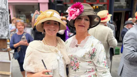 A mother and her daughter wearing long Edwardian inspired dress and elaborate hats 