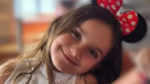 Aria Thorpe. She has long dark hair and is wearing Minnie Mouse ears. Her head is tilted to the side and she is looking directly at the camera and smiling.