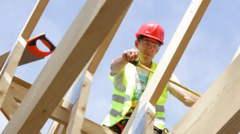 Getty Images Fluorescent Yellow vest and a builder that measures struts for a roof of a hard hat. Stops on struts and draws photos from below. 