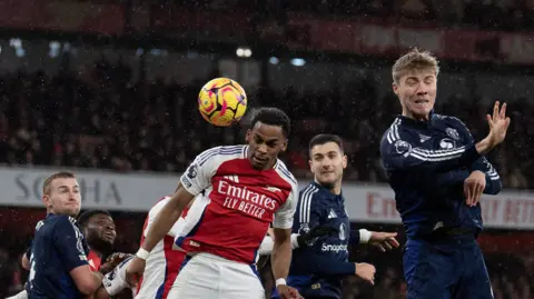 Jurrien Timber opens the scoring for Arsenal. He is heading the ball while Manchester United players are nearby.