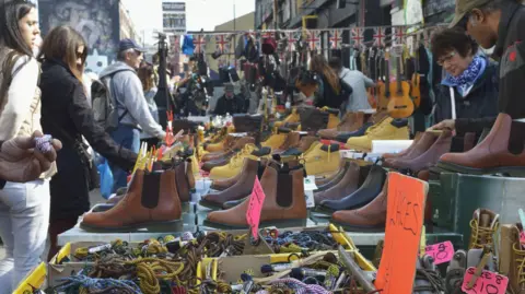 Getty Images A market stall with many pairs of leather boots on display and passers by